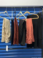 Six Chicos clothing items hung on a rack showing various pants and skirts in beige, rust, black colors.