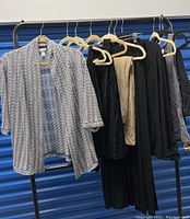Clothing on rack including light grey cardigan/jacket, assorted pants, skirts, and tops in black, beige and grey tones.