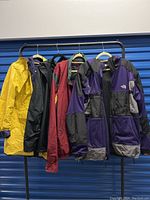 Full view of five men's coats hanging on rack labeled as XL/XXL sizes including The North Face, English Squire, Under Armour.
