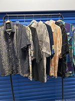 Eight silky men's camp shirts hanging on rack, showing various prints and colors.