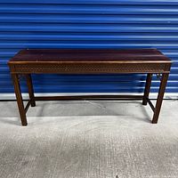 Full view of vintage wooden sofa console table showing carved decorative border and tapered legs, placed against a blue storage door.