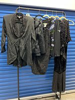 Full view of 9-piece lot of black women's dressy garments on hangers showing variety of jackets, dresses, sweaters, and tops.