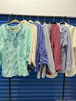 Eight women's tops hanging on a black metal rack, showing variety in color and style.