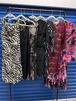 Full view of 8 garments including 7 dresses and 1 matching jacket in various colors and patterns hung on hangers on a rack.