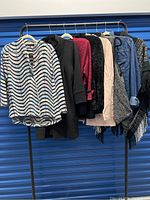 Full view of eight women's jackets and cardigans hanging on a rack, showing a variety of fabrics, colors, and textures
