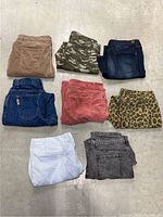 Eight pairs of women's pants, sizes 14/16, folded on floor showing various colors and styles including denim, leopard print, pink, white, and camouflage.