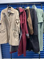 Five vintage women's trench coats hanging on a rack showing variety of colors and styles.