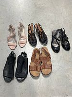 Five pairs of women's shoes and sandals in various styles and colors laid out on concrete floor