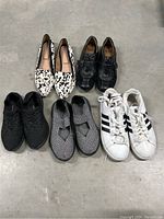 Five pairs of women's shoes arranged on a gray surface including flats and sneakers from Adidas, Sofft, and Bernie Mev.
