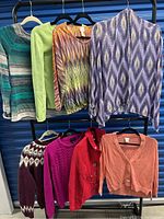 All 8 sweaters and tops on hangers, showing front view of each garment in different colors and patterns.