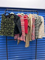 Ten women's tops, jackets, and one cardigan with matching pants hanging on a clothing rack, showing various colors and patterns