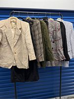 Photo of six jackets on hangers including beige, plaid, olive green, plaid with red accents, black, and blue striped shirt/jacket