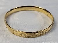 Close-up image showing overall exterior of the carved gold filled bracelet with floral and swirl design, set on a white cloth background.