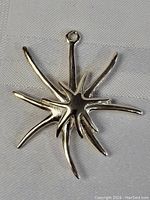 Close-up photo of a shiny 925 sterling silver pendant with an abstract starburst design lying on a white fabric surface.