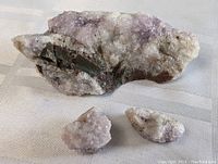 Three raw amethyst crystal specimens displayed on a white textured cloth, showing the varied sizes and crystal clarity.