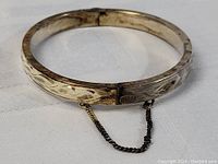 Close-up image of the thick sterling silver carved bracelet showing the carved pattern and part of the linked safety chain.