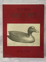 Front cover of the book Ontario Decoys II by Bernie Gates showing the title and a black and white image of a duck decoy on a red background.