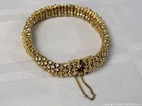 Photo showing the full bracelet laid flat to display design, gold plating, rhinestone encrusted detailing, and safety chain clasp.