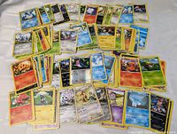 Photo showing approximately 50 Pokemon trading cards spread out to display a variety of cards including multiple types and species.