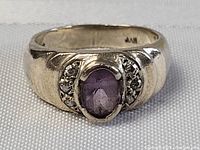 Front-facing close-up of chunky sterling silver ring with a central oval amethyst and small clear accent stones.