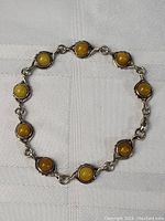 Full view of vintage sterling silver bracelet laid out on white fabric showing ten yellow to amber brown stone settings.