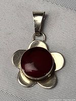 Front view of sterling silver flower-shaped pendant with round red coral stone centerpiece showing polished, shiny surface.