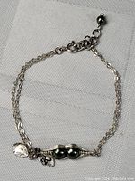 Top view of full sterling silver chain bracelet with pea pod centerpiece and attached charms on a white textured cloth background.