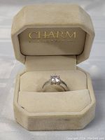 Ring displayed inside beige Charm Diamond Centres box showing ring front and central diamond.