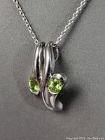 Close-up of the sterling silver pendant featuring two oval peridot stones in a modern double loop design.