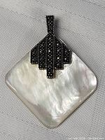 Front of the pendant showing mother of pearl base and sterling silver with marcasite stones in geometric pattern.