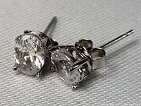 Close-up photo of one sterling silver stud earring showing the round clear faceted stone and four-prong setting, and the post and butterfly backing.