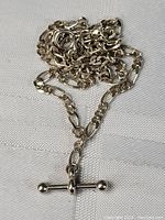 Close-up photo of the sterling silver necklace chain and T-bar clasp laid on fabric, showing chain detail and clasp design.