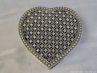 Heart-shaped metal dresser box top view showing encrusted lattice design and studded border.