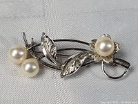 Front angled view showing floral design, leaves with textured detail and three faux pearls of varying sizes