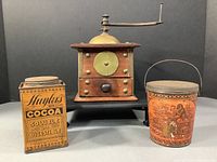 Photo showing the antique wood and brass coffee grinder centered, with the Huyler's rectangular cocoa tin on the left and the Schepps round cocoa-nut tin on the right.