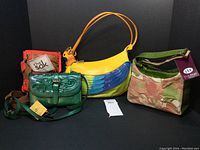 Photo showing the full lot of four handbags including vibrant parrot design, green leather bag, floral fabric purse with green trim, and tan/red shoulder bag.