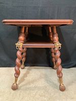 Front view of the entire occasional table showing twisted wood legs with brass claw feet and brass wolf head details.