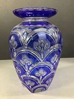 Front angle showing detailed cut floral and shell designs on cobalt blue crystal vase with scalloped rim.