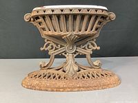 Side view of cast iron base showing ornate open lattice and scrollwork design with rust patina