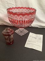 Photo showing large Czech cranberry glass compote bowl, decorative cranberry etched vase, and a document on the side for provenance or authenticity.