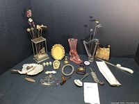 Overview of lot with hat pin holders containing decorative pins, glass boot vase, frames, dish, enameled box, chain, pencils, spoon and opener