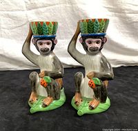 Front view of the pair of ceramic monkey candle holders with detailed facial features and colorful leaf-patterned cups.