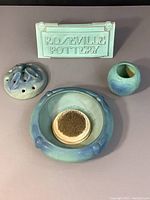 Overview of all five items: Van Briggle pottery pieces and Roseville Pottery sign on gray surface