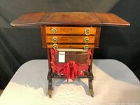 Full frontal view of the sewing table with drop leaf top opened showing drawer fronts and silk pouch underneath.