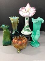 Five-piece lot arranged on gray surface: Northwood footed rose bowl front center, Loetz bud vase front left, Fenton green hobnail vase front right, Northwood three-legged vase back left, Fenton hand-painted lily bud vase back center