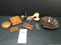 Overall view of nine-piece tobacciana set laid out on a black surface showing the variety of wood cases, glass snuff bottle, pipes, metal lighter case, brass trinket case, and ashtray.