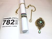 Group shot of brooch pendant, ring on rolled paper, rope chain with pendants