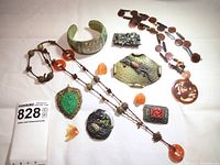 Overview of 11 pieces laid out: necklaces, brooches, pendants, cuff bracelet
