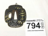 Front view of mokko-shaped tsuba showing pagoda, bridge, waterwheel in high relief with gold accents on nanako background.