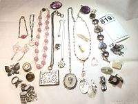 Photo showing a variety of vintage jewelry items including necklaces with pink beads, pendants, brooches, earrings, and rings, laid out on a white surface.